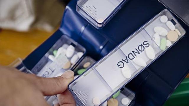 En hånd tager en pilleæske med medicin, der er organiseret i en doseringsæske med etiketten "SØNDAG".