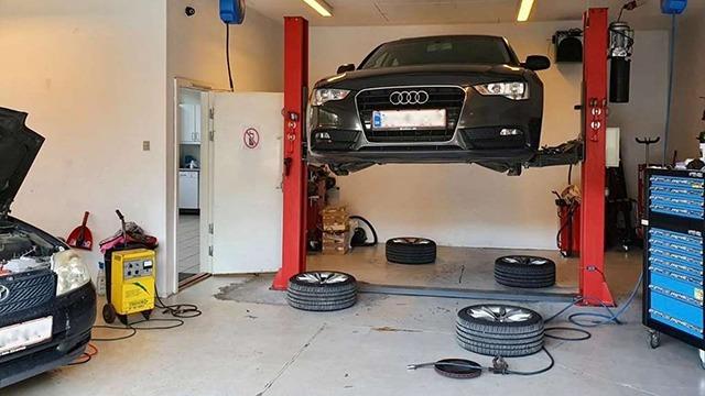 En sort Audi hævet på en lift i et værksted med dæk og værktøj synligt i baggrunden.