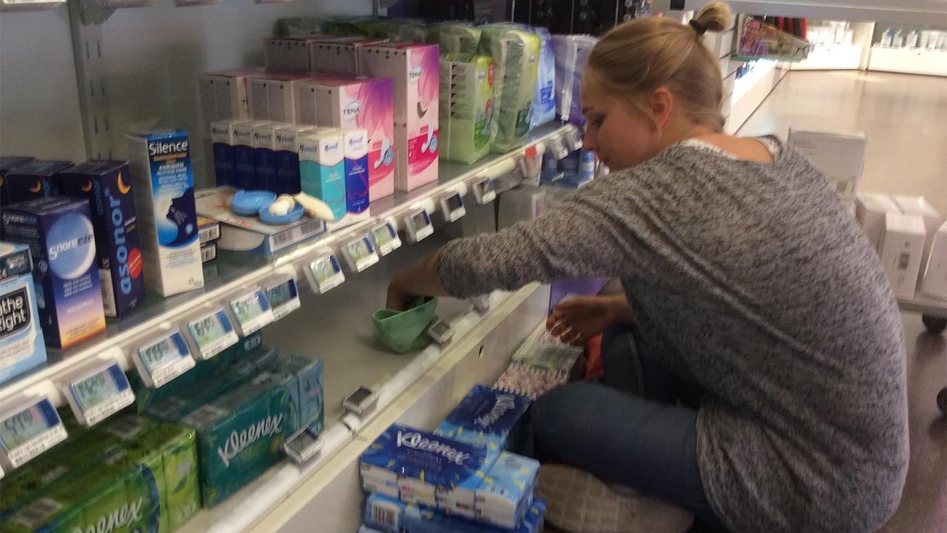 En kvinde organiserer produkter på en hylde i en butik, mens hun sidder på hug.