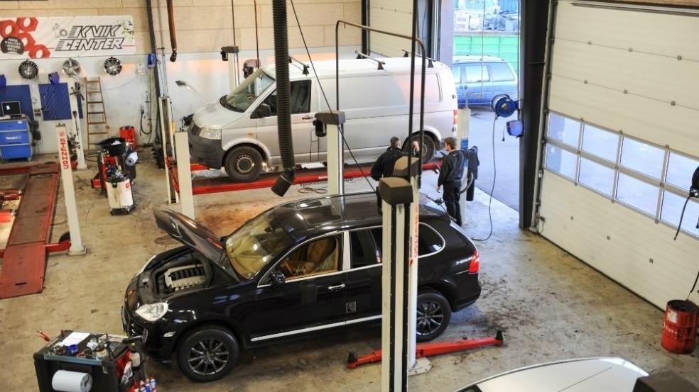 Billede af et autoværksted med flere biler på lifte og mekanikere, der arbejder på reparationer.