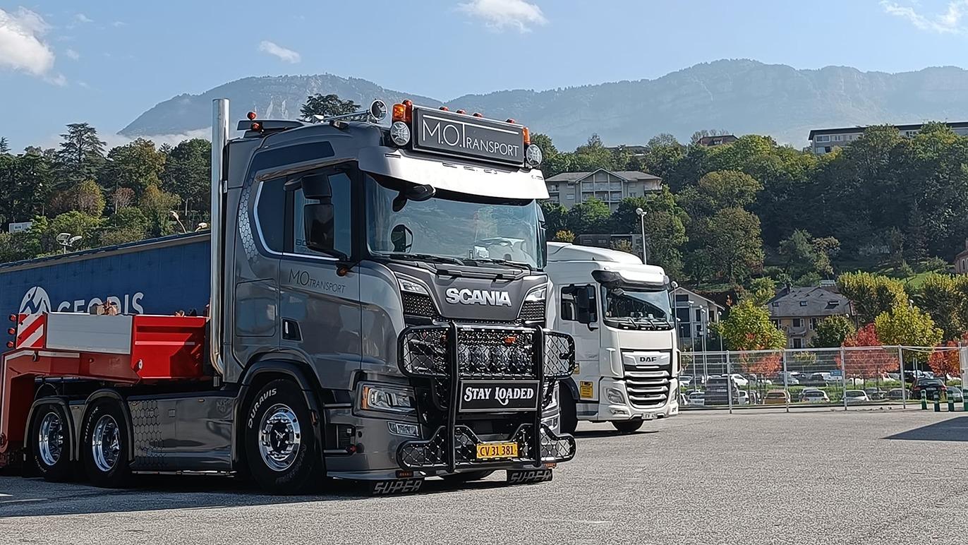 En sort Scania lastbil parkeret med en container i baggrunden og bjerge i horisonten.