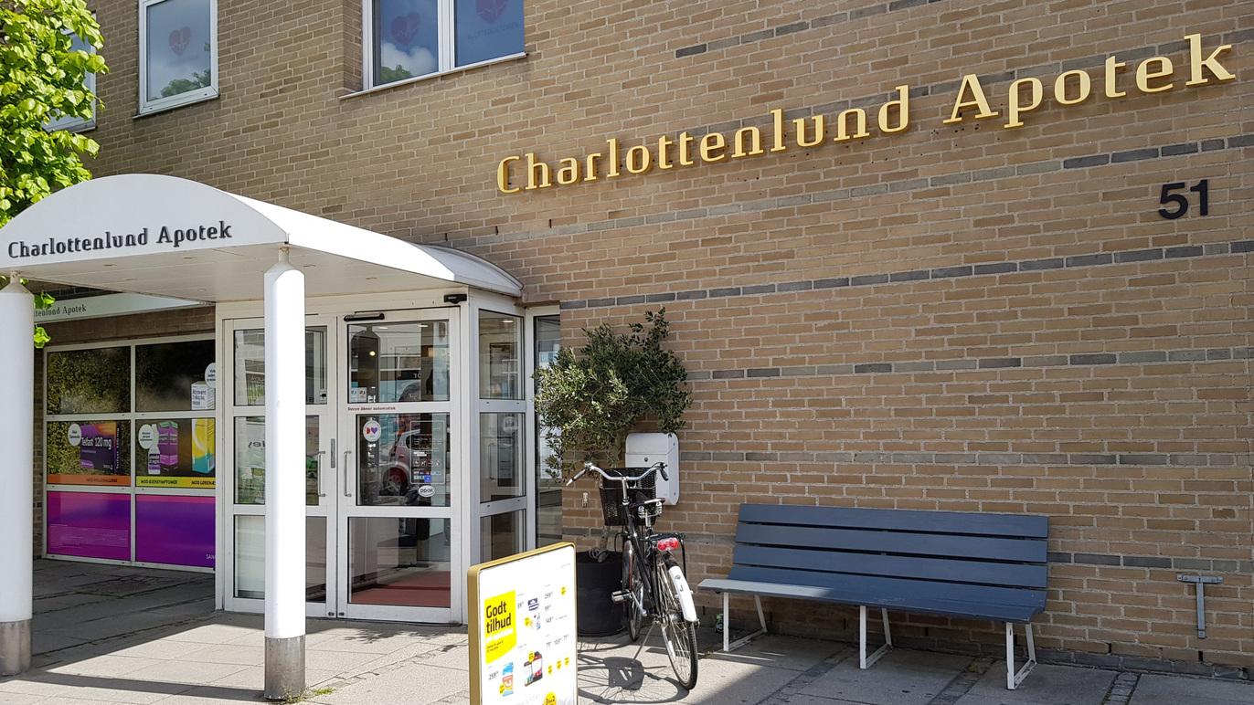 Indgangen til Charlottenlund Apotek med en bænk og en cykel foran bygningen.