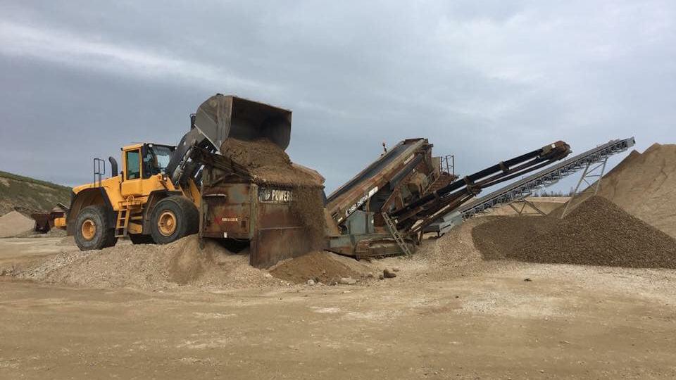 En stor gravemaskine læsser sand i en lastbil på en byggeplads med grus og sandbunker.