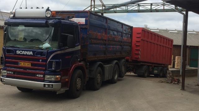 En Scania lastbil med en blå og rød container, der bakker ind i en lagerbygning.