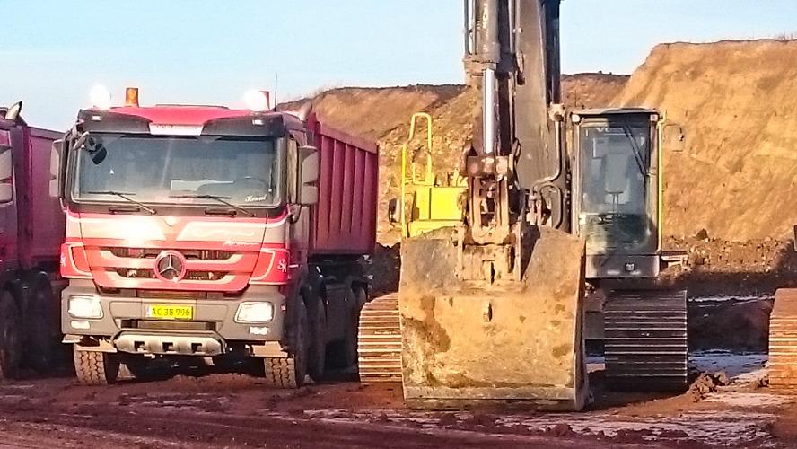 En stor gravemaskine arbejder ved siden af en lastbil på en byggeplads med jord og sand.