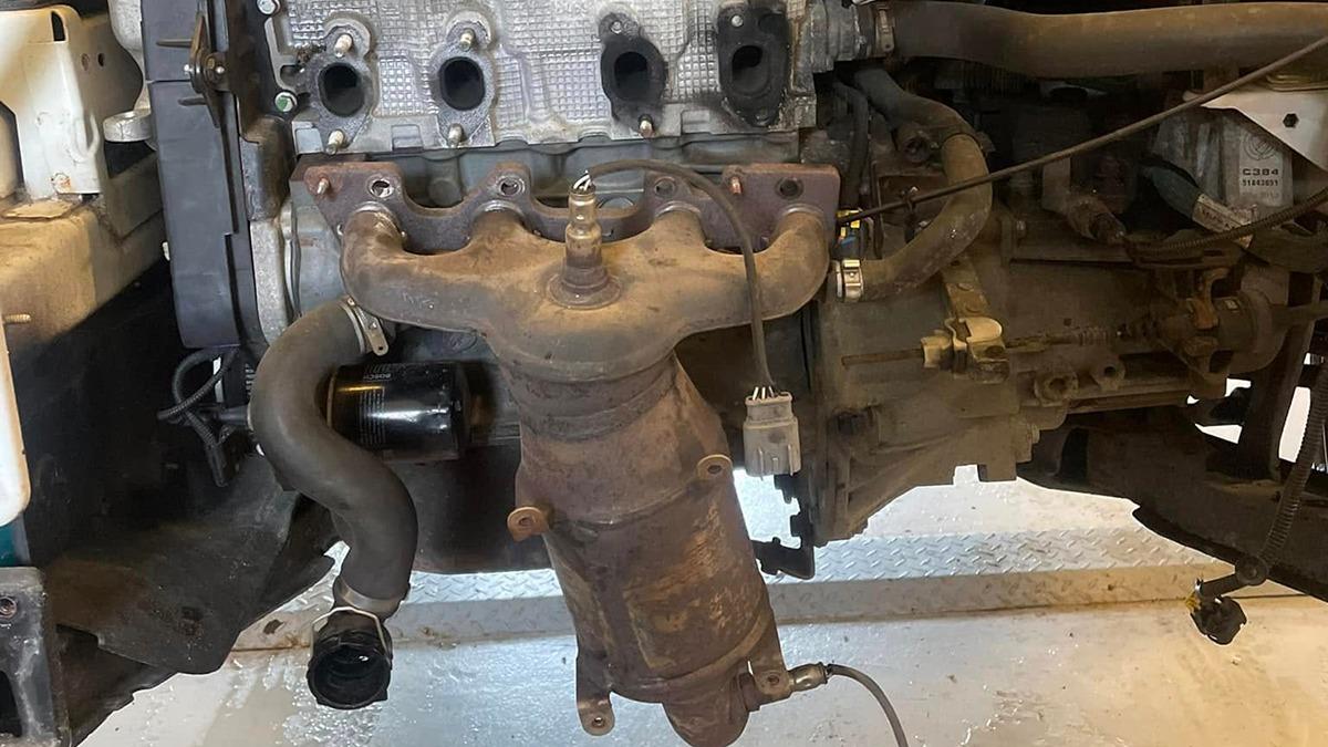 Billede af en bilmotor med udstødningsmanifold og tilslutninger, der viser detaljer om motorens komponenter.