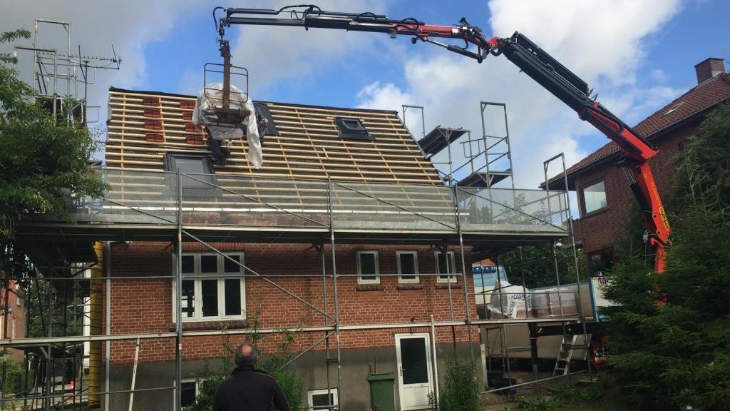 Hus med stillads og kran, der arbejder på taget, under renovering i et boligområde.