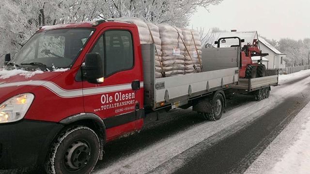 Rød lastbil med en trailer, der transporterer sække, kører på en sneklædt vej.