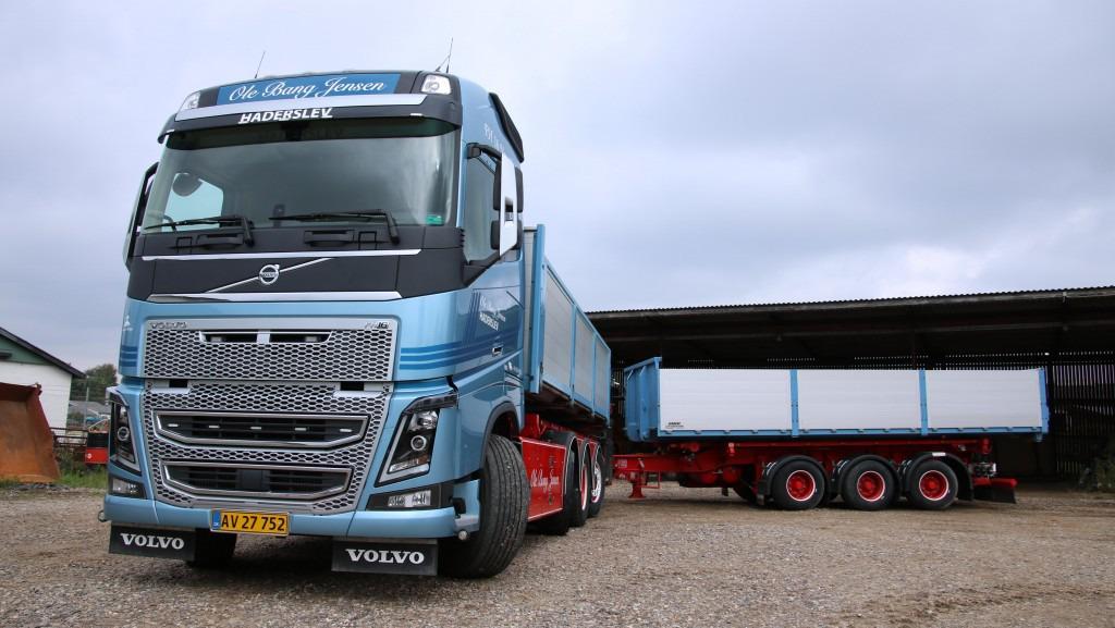 En blå Volvo lastbil parkeret ved en lade med en stor trailer bagpå.