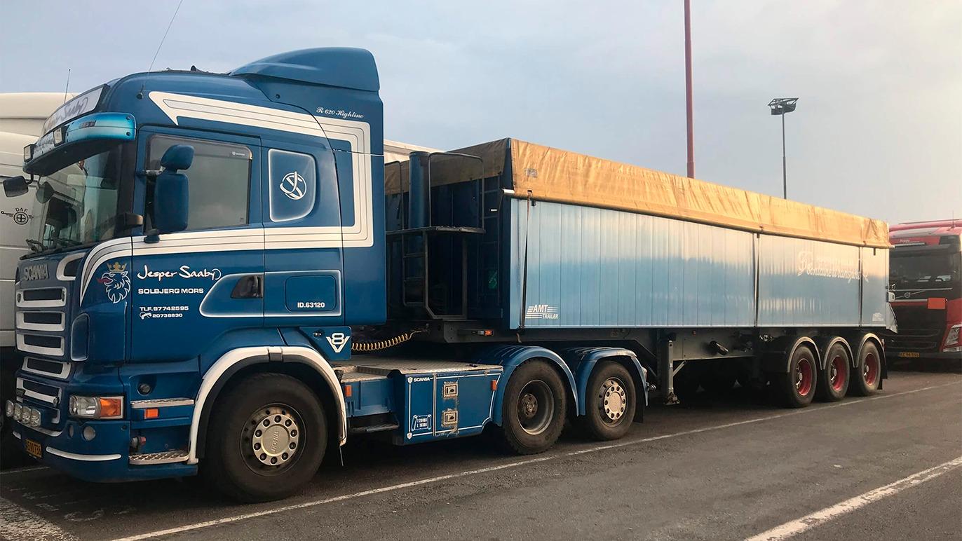 En blå lastbil med en orange presenning parkeret på en rasteplads.