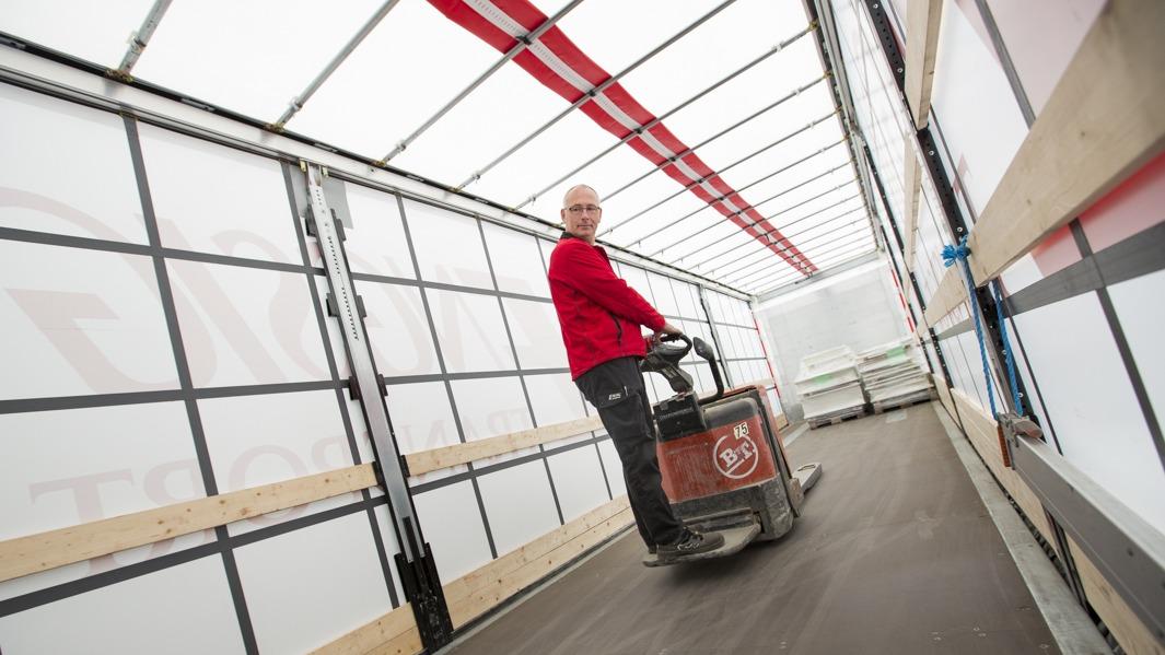 En mand i rød trøje kører en palletruck i en lastbil med gennemsigtige vægge.