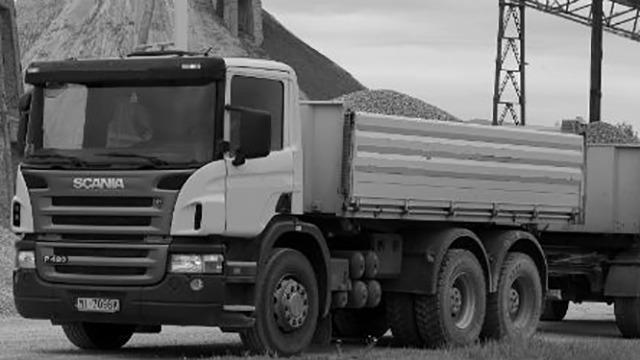 En sort-hvid lastbil fra Scania, der transporterer grus ved en byggeplads.