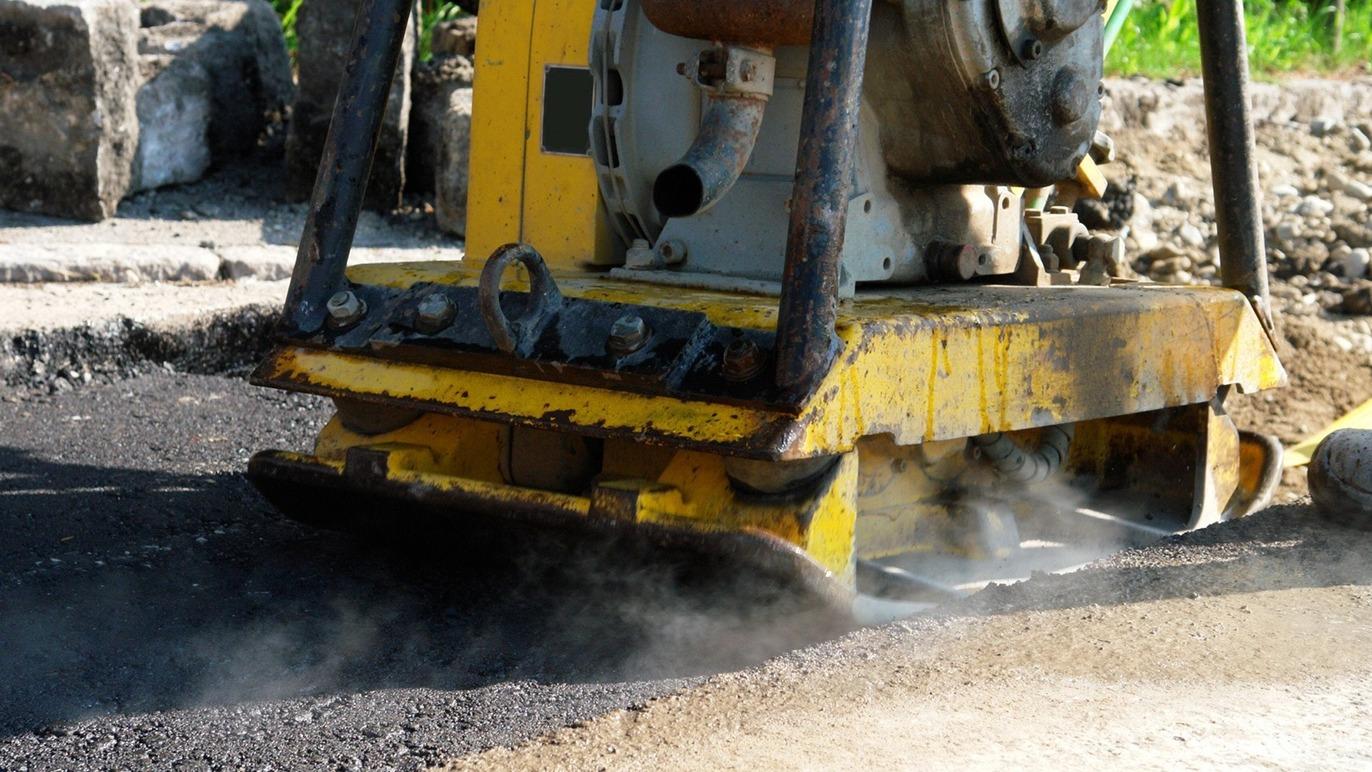 En gul asfaltvibrator arbejder på en vej, mens damp stiger op fra den varme asfalt.