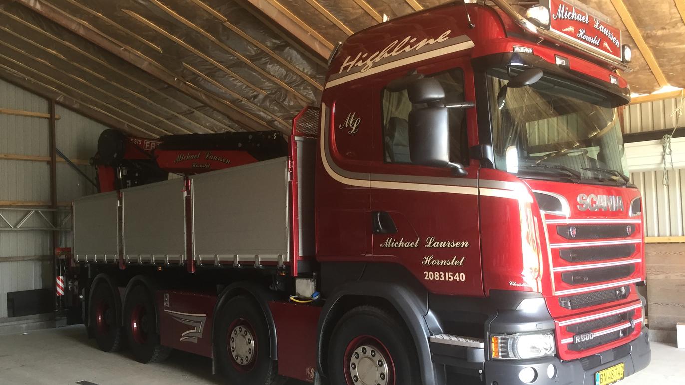 En rød Scania lastbil parkeret i en lade med træloft og metalvægge.