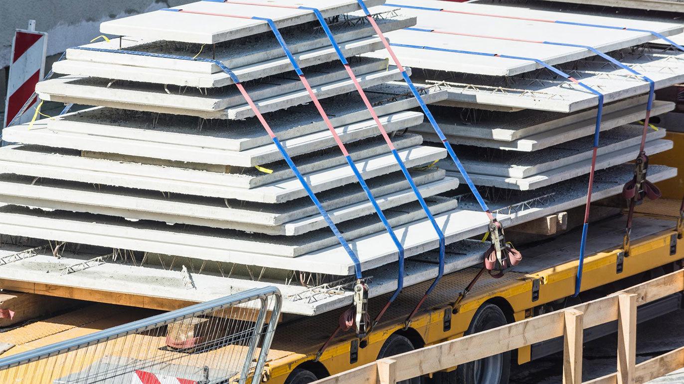 Lastebil med stablede betonplader sikret med stropper på en byggeplads.
