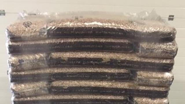 Stablede sække med træpiller pakket i plastfolie i et lagerområde.