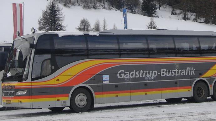 En bus fra Gadstrup Bustrafik parkeret i sneen med træer i baggrunden.
