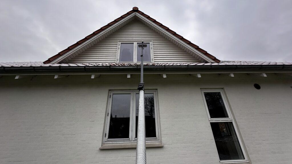 Hus med skråtag og vinduer, set fra jorden, med en stang der strækker sig op mod taget.