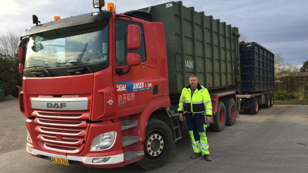 En rød DAF lastbil med en stor container og en mand i arbejdstøj står ved siden af.