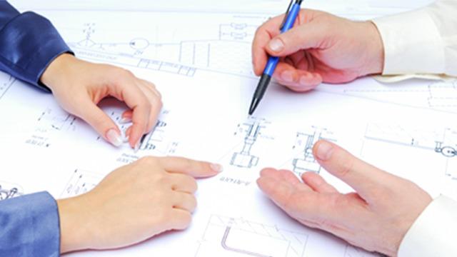 Hænder, der arbejder på tekniske tegninger med en pen og peger på detaljer i designet.