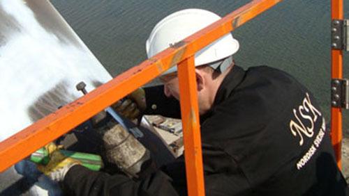En håndværker arbejder på en stige ved en bygning, iført hjelm og arbejdstøj, mens han svejser.
