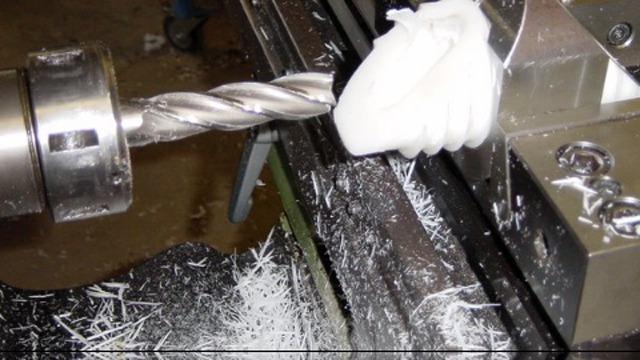 Billede af en metalfræser med en spiralbor, der skærer i en hvid plastdel med spåner omkring.