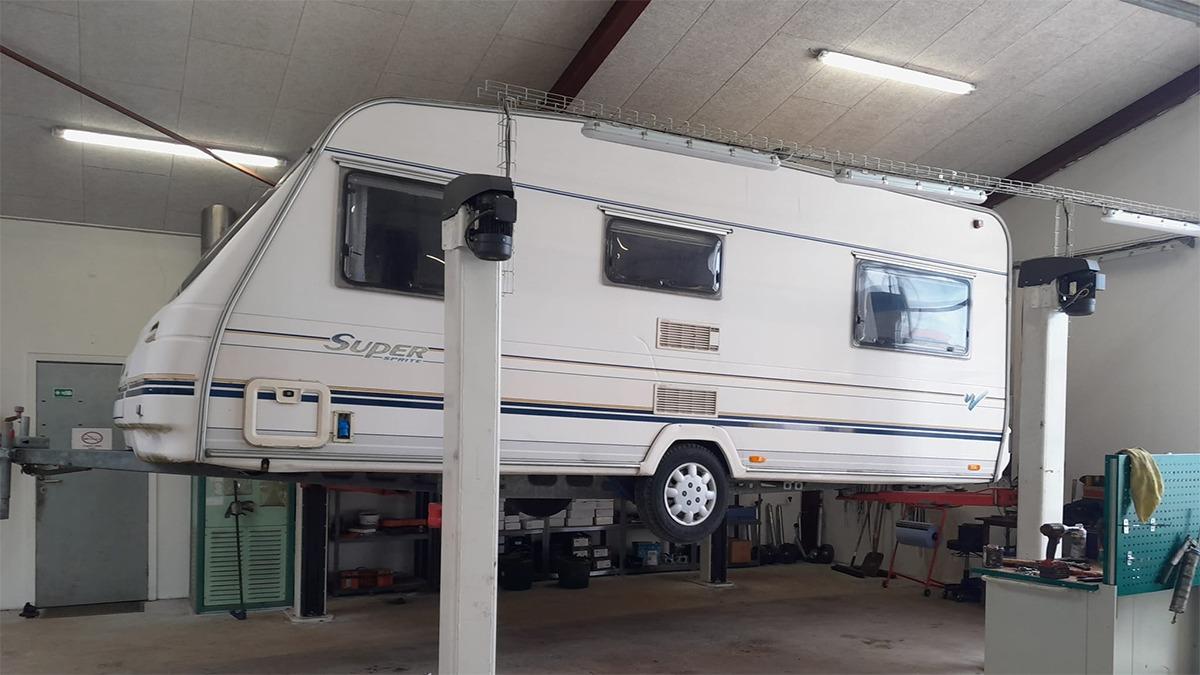 En hvid campingvogn hævet på en lift i en garage med lys i loftet.