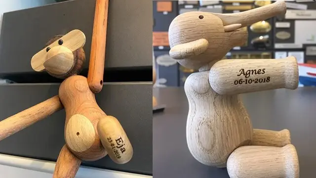 To træfigurer, en abe og en elefant, med indgraverede navne og datoer, placeret på en sort overflade.