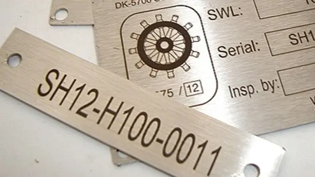 Et metalmærke med serienummer SH12-H100-0011 og en cirkel med et hjuldesign.