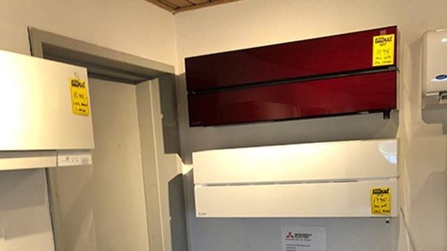 Vægmonterede klimaanlæg i forskellige farver, herunder rød og hvid, udstillet i en butik.