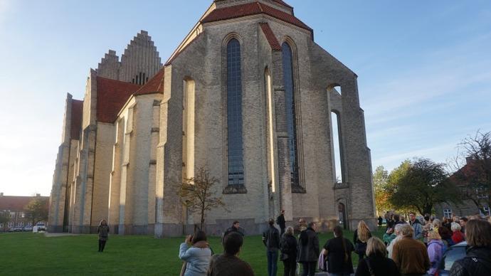 En gruppe mennesker står foran en stor, historisk kirke med høje vinduer og en rød tag.