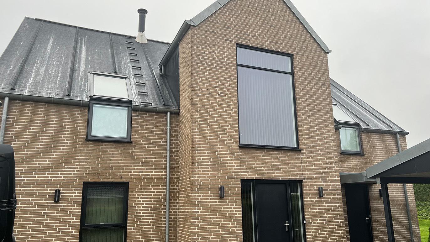 Moderne murstenshus med skråtag og store vinduer, beliggende i et roligt område.