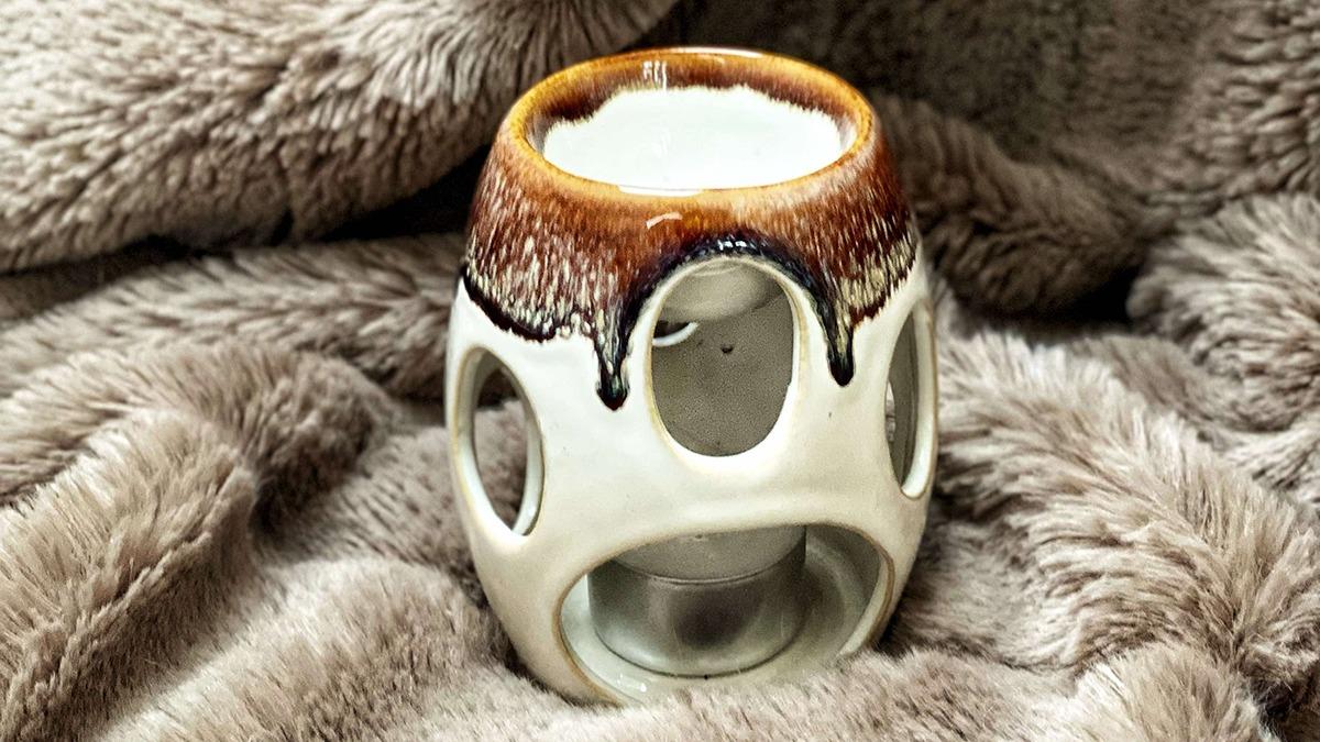 En keramisk duftlampe med en brun glasur, placeret på en blød, grå pels.