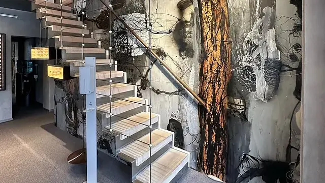 Moderne trappe i træ med metalgelænder, omgivet af en kunstnerisk vægdekoration med abstrakte mønstre.