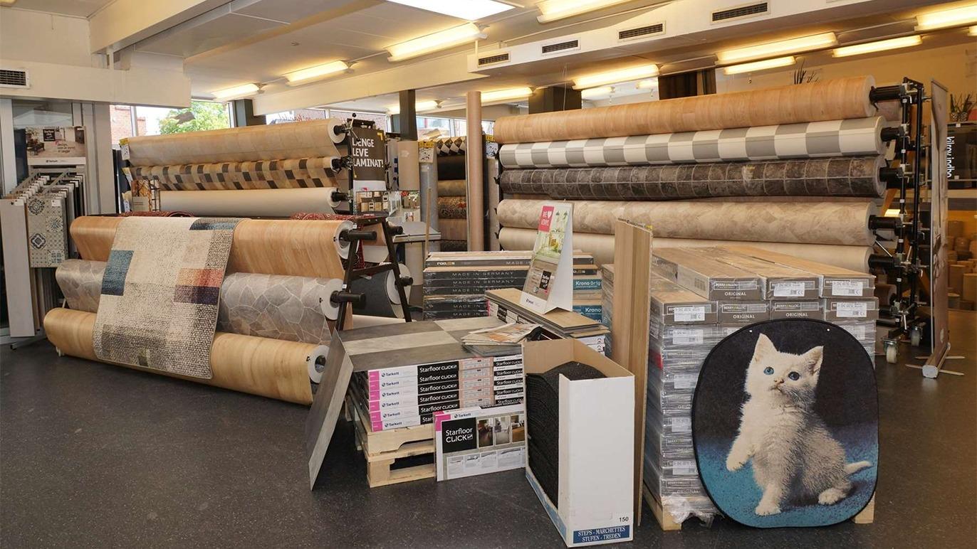 Ruller af tapet og gulvbelægning i en butik med en katteplakat og forskellige udstillingsmaterialer.