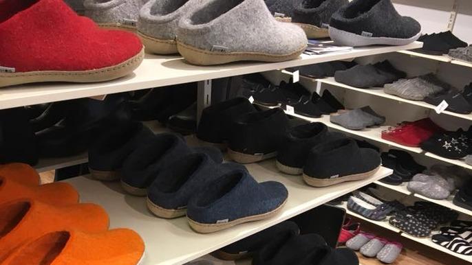 Hylder med forskellige farvede hjemmesko, herunder grå, sort, rød og orange, i en skobutik.