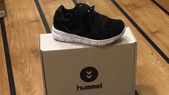 Sort hummel sneakers på en hvid kasse med hummel-logo, placeret på et trægulv.