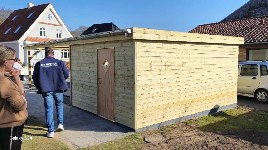 Nybygget træskur med en dør, beliggende på en græsplæne ved en bolig.