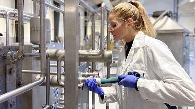 En kvinde i laboratoriefrakke arbejder med rør og udstyr i et moderne laboratorium.