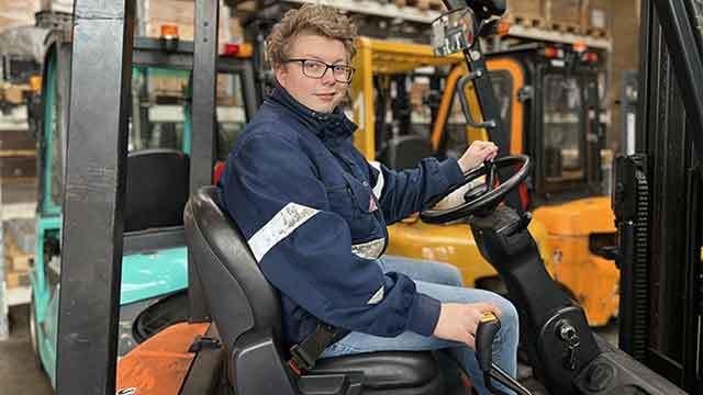 En person sidder i en gaffeltruck i et lager med flere gaffeltrucks i baggrunden.