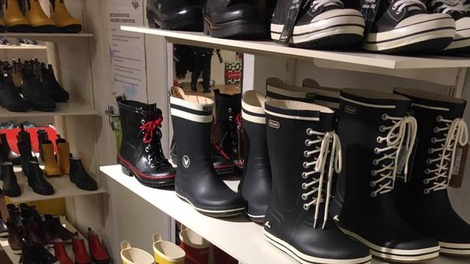 Forskellige gummistøvler i en butik, herunder sorte og farverige modeller på hylder.