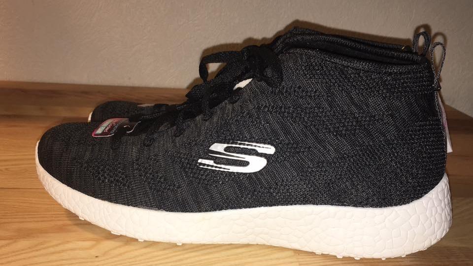 Sorte sneakers med hvidt logo fra Skechers, placeret på en træoverflade.