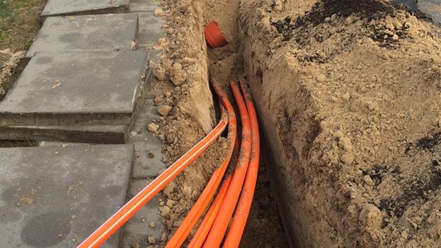 Gravet grøft med orange kabler, der ligger i sandet, ved siden af betonfliser.