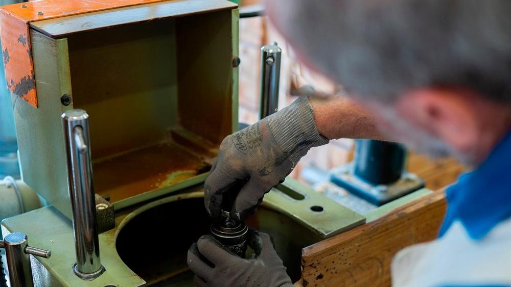 En person iført handsker arbejder med en maskine, mens de installerer en komponent i en metalbeholder.