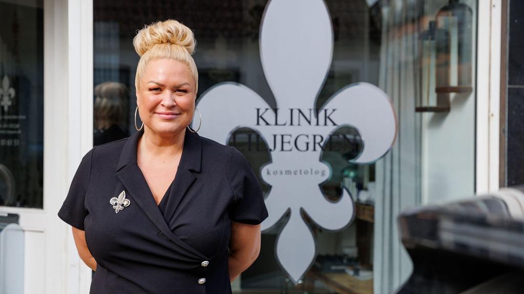 Kvindelig ejer står foran Klinik Højgaard med en blomsterlignende logo i baggrunden.