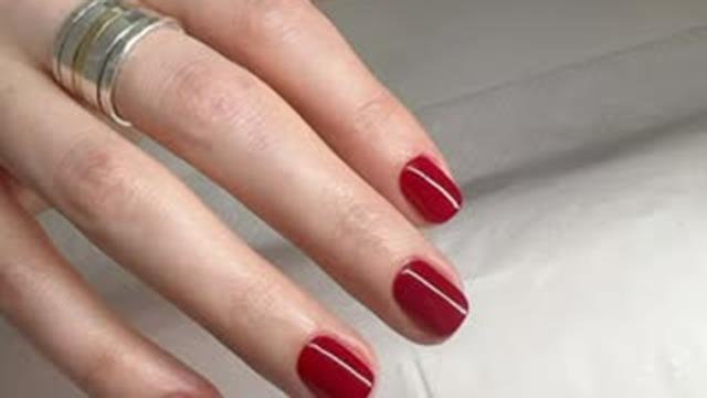 En hånd med rød neglelak og en sølvring på fingeren, der viser en elegant manicure.