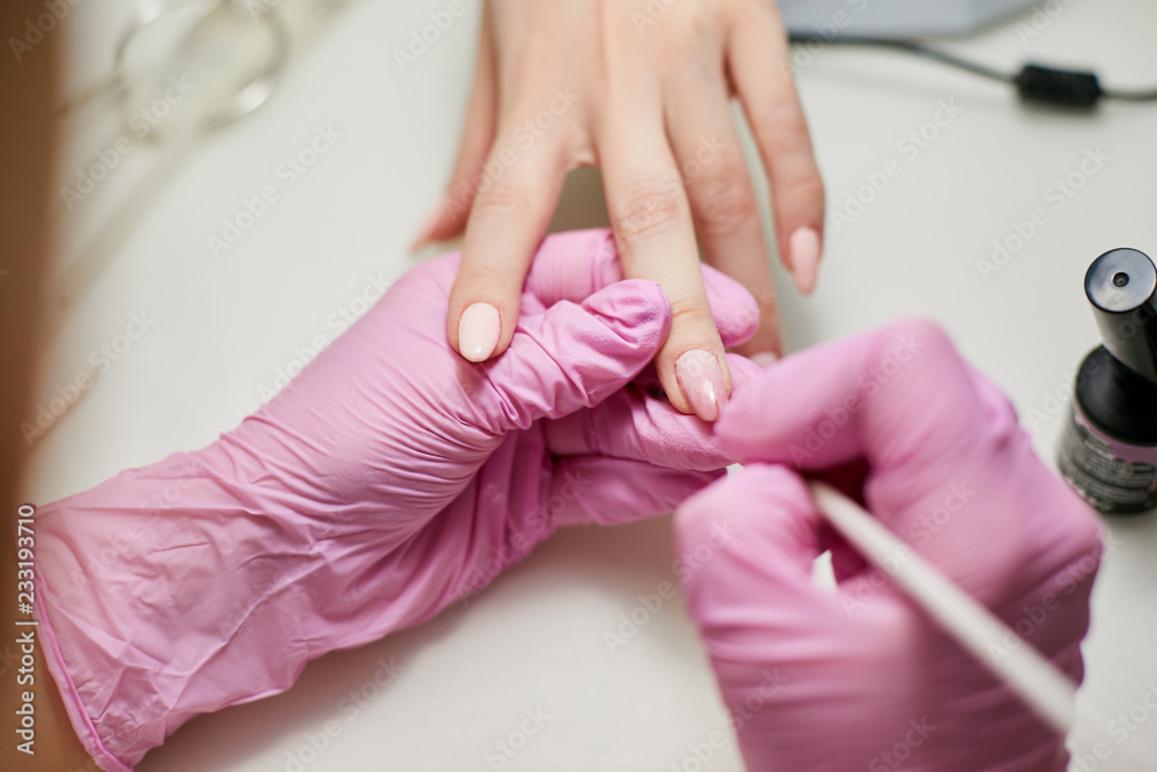 En person får manicure med lyserøde negle, mens en anden person arbejder med neglelak.