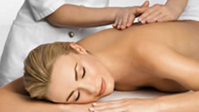 En afslappet kvinde får massage på ryggen af en behandler i hvidt tøj.