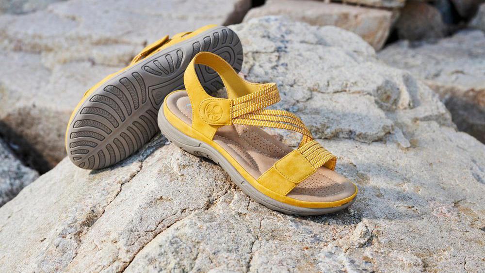 Gule sandaler med remme, placeret på klipper ved vandet, ideelle til sommerudflugter.