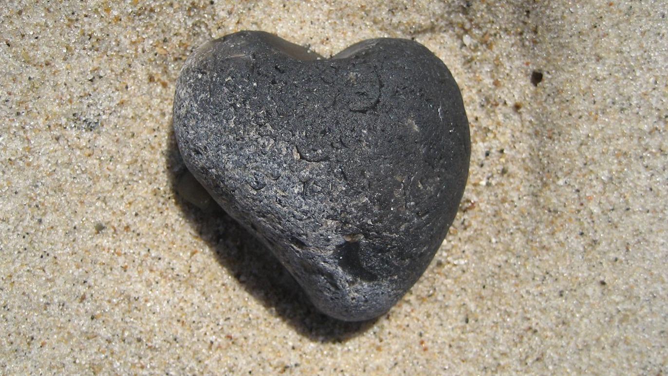 En hjerteformet sort sten på sandet strand.